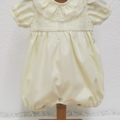 Macacão de bebé creme com folho rendado na gola em manequim de madeira