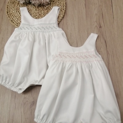 Dois macacões de bebé brancos com detalhes em ponto smock e botões em fundo de madeira