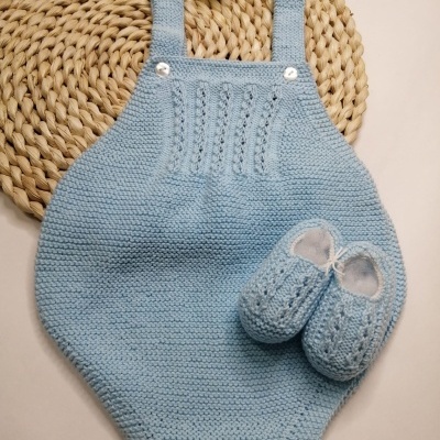 Macacão azul claro de malha para bebé com sapatinhos à frente sobre tapete redondo trançado
