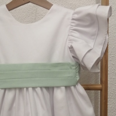 Vestido branco com faixa verde claro pendurado num cabide de madeira