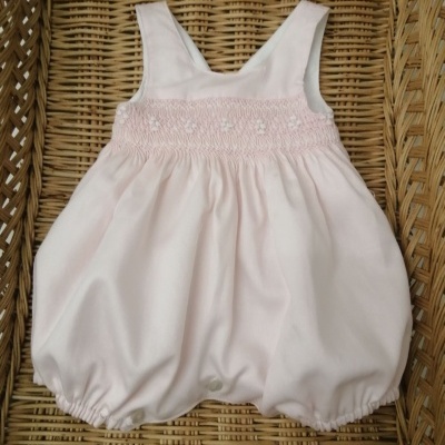 Macacão de bebé rosa claro com bordado floral, colocado numa cesta de vime.