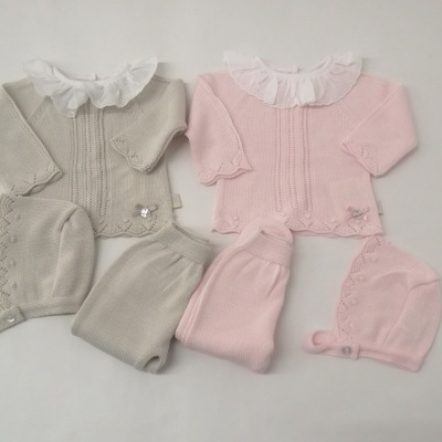 Dois conjuntos de roupa de bebé tricotada com camisolas, calças e gorros, em cinza claro e rosa claro, com golas brancas frugadas.