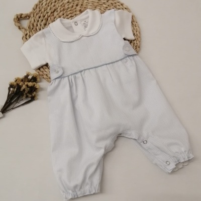 Macacão de bebé azul claro e branco sobre tapete trançado com flores secas