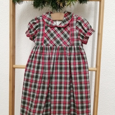 Vestido de criança xadrez vermelho verde branco pendurado numa estrutura de madeira com decoração de pinhas