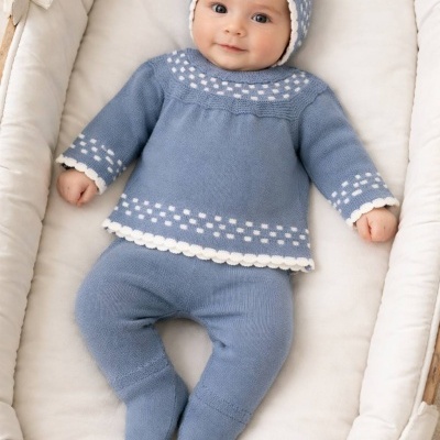 Bebé deitado em almofada branca a usar conjunto de tricô azul com detalhes brancos