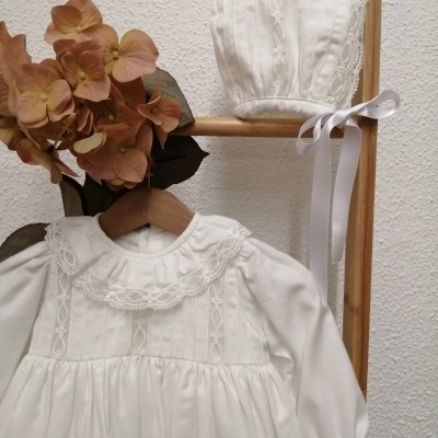 Vestido branco de bebé com renda e gorro branco com renda ao fundo de parede texturada