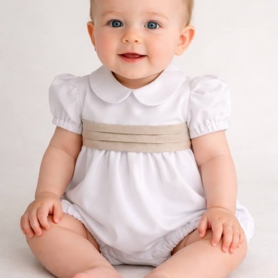 Bebé sentado com roupa branca e faixa bege