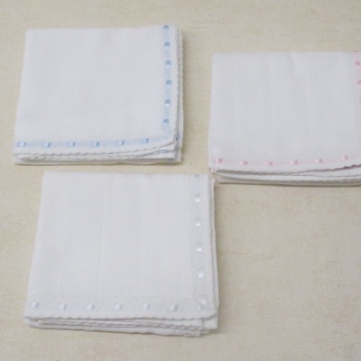 Três conjuntos de lenços brancos com bordas coloridas sobre superfície clara