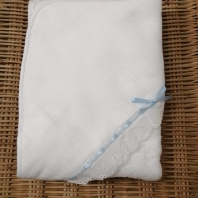 Toalha branca com renda e fita azul sobre superfície de rattan