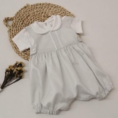 Macacão curto de bebé branco com riscas cinza e detalhes botões sobre tapete natural e flores secas