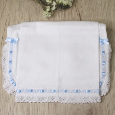 Lenço branco com bordado de renda e fita azul sobre mesa de madeira