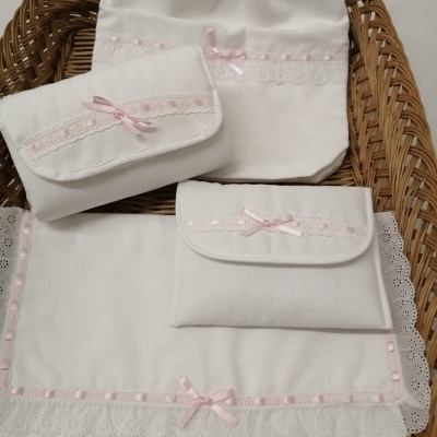 Conjunto de tecidos brancos com renda e laços cor de rosa dentro de cesta de vime.