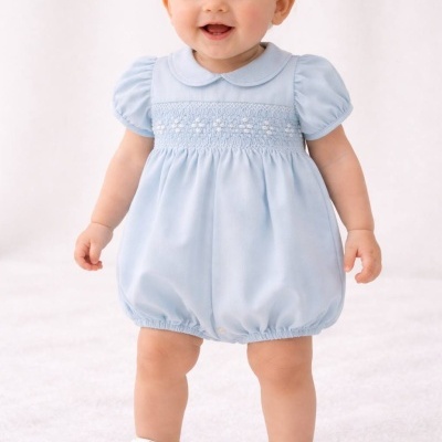 Bebé com macacão azul claro e sapatos brancos em fundo branco