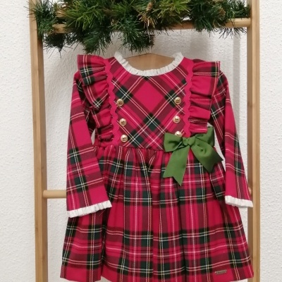 Vestido infantil tartã vermelho com folhos, botões dourados e fita verde, pendurado em estrutura de madeira decorada