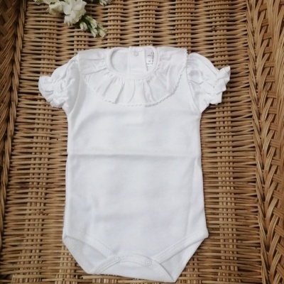 Body branco de bebé com gola e mangas franzidas sobre cesta de verga com flores ao lado.