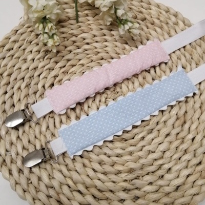 Suportes para chupetas rosa e azul claro com clipes metálicos sobre placemat de corda com flores brancas