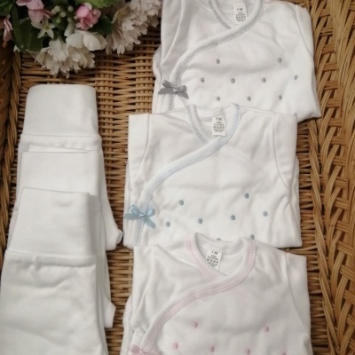 Conjunto de bodies brancos com bordados e calças brancas sobre superfície de vime com flores artificiais