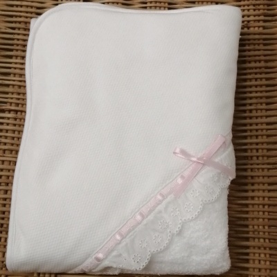 Toalha branca com canto em renda e laço rosa sobre superfície de vime