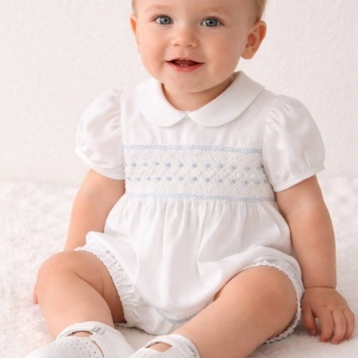 Bebé com roupa branca e sapatos brancos sentado numa superfície macia branca