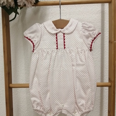 Macacão curto branco com pontos pretos e detalhes vermelhos pendurado em cabide de madeira