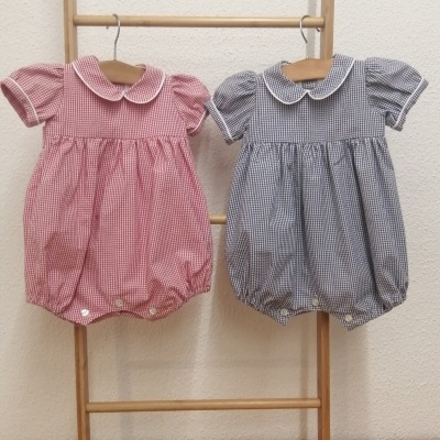 Dois macacões de bebé xadrez rosa e azul escuro pendurados em escada de madeira sobre fundo bege