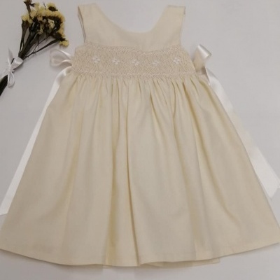 Vestido infantil bege com bordado branco e ramo de flores secas ao lado