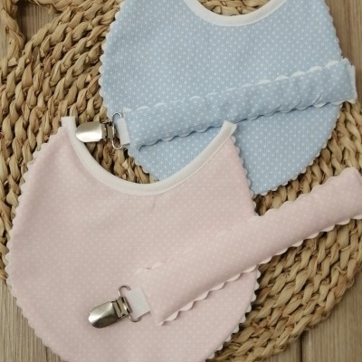 Dois babetes redondos azul e rosa claro com porta-chupetas sobre base de madeira e passadeira de fibra natural