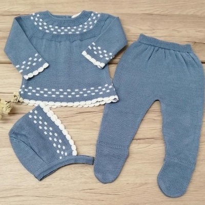 Conjunto de roupa para bebé azul em malha com detalhes brancos sobre superfície de madeira clara