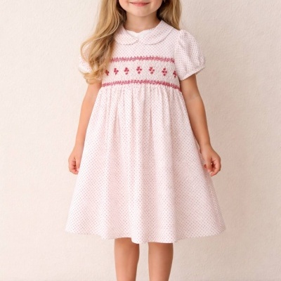 Menina com vestido rosa claro com pontos e bordado vermelho usando sapatos brancos