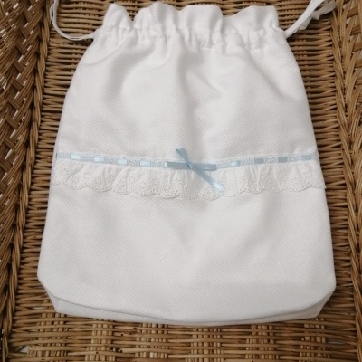 Saco branco com fita azul e renda sobre superfície de verga trançada