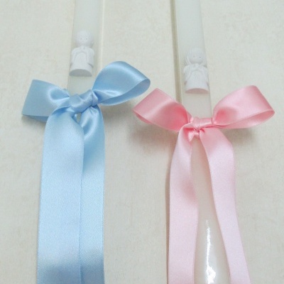 Duas velas brancas com figuras de anjos e laços de cetim azul e rosa