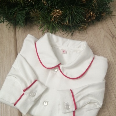 Camisa branca de algodão com detalhes vermelhos e botões brancos dobrada sobre madeira com decoração natalícia