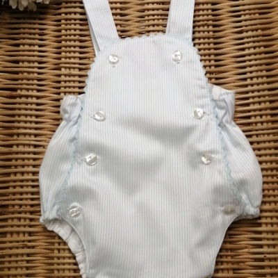 Macacão de bebé branco com riscas azuis e botões sobre superfície de vime