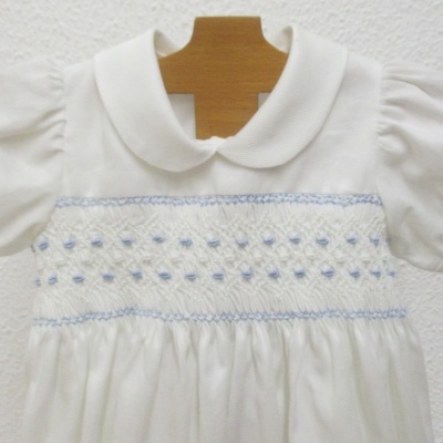 Vestido branco com bordados azul claro pendurado num cabide de madeira