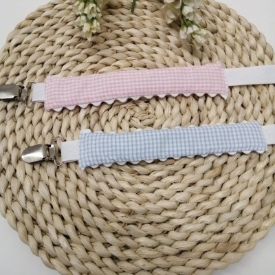 Suspensórios rosa e azul com padrão vichy sobre tapete redondo de fibras naturais trançadas.