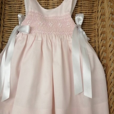 Vestido bebé rosa claro com laços de cetim branco em fundo rústico