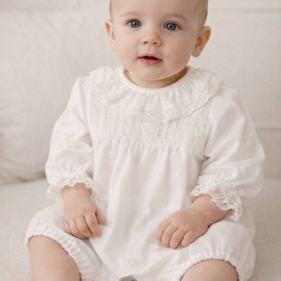 Bebé com macacão branco de renda sentado