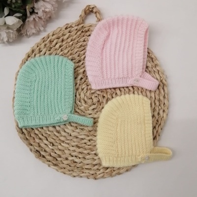 Três gorros infantis coloridos sobre tapete de fibras naturais com flores ao lado