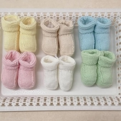 Seis pares de botins de bebé em malha de várias cores numa bandeja branca com padrão vazado