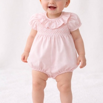 Bebé de pele clara com fato de banho rosa e sapatos brancos num fundo branco.