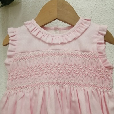 Vestido cor-de-rosa claro para bebé com franzidos e folhos pendurado num cabide de madeira