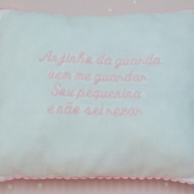 Almofada branca com bordado rosa e texto em português em fundo rosa com corações brancos