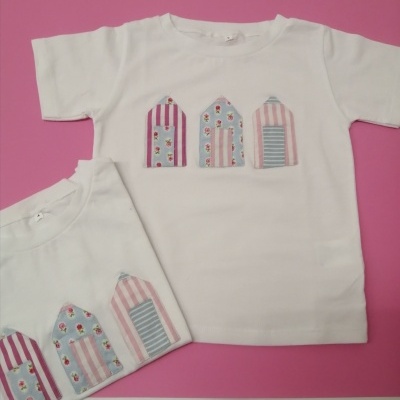Duas t-shirts brancas para criança com padrões coloridos de casas de praia aplicados