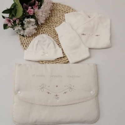 Conjunto de roupa de bebé branco com bolsa e flores sobre fundo branco