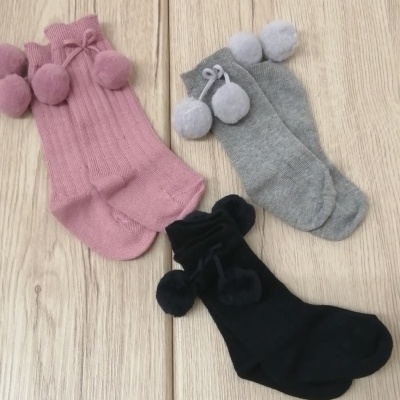 Três pares de meias coloridas com pompons sobre chão de madeira clara