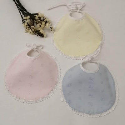 Três babetes redondos de bebé em amarelo, rosa e azul com borda rendada e fitas para amarrar.