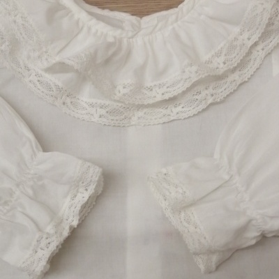 Blusa branca com gola e punhos de renda sobre madeira clara