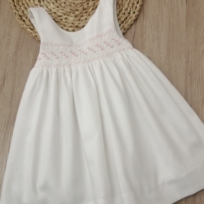 Vestido branco com bordado rosa sobre madeira clara e tapete de palha