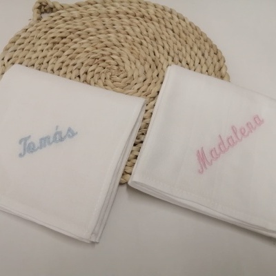 Dois panos de boca brancos com bordados com nomes em azul e rosa sobre base trançada.