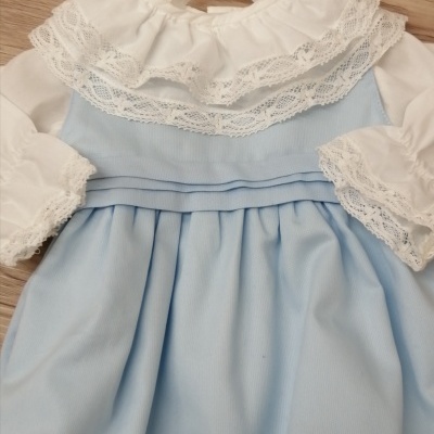 Vestido infantil branco e azul com rendas e pregas pendurado